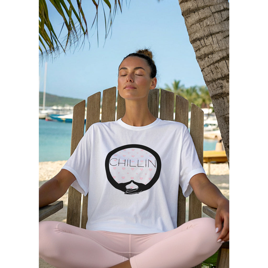 Woman sitting outdoors in Adirondack chair by a beach, wearing a white t-shirt with 'CHILLIN' graphic design.