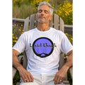 Man sitting outdoors in a wooden Adirondack chair wearing a white t-shirt with 'Laid Back' graphic design