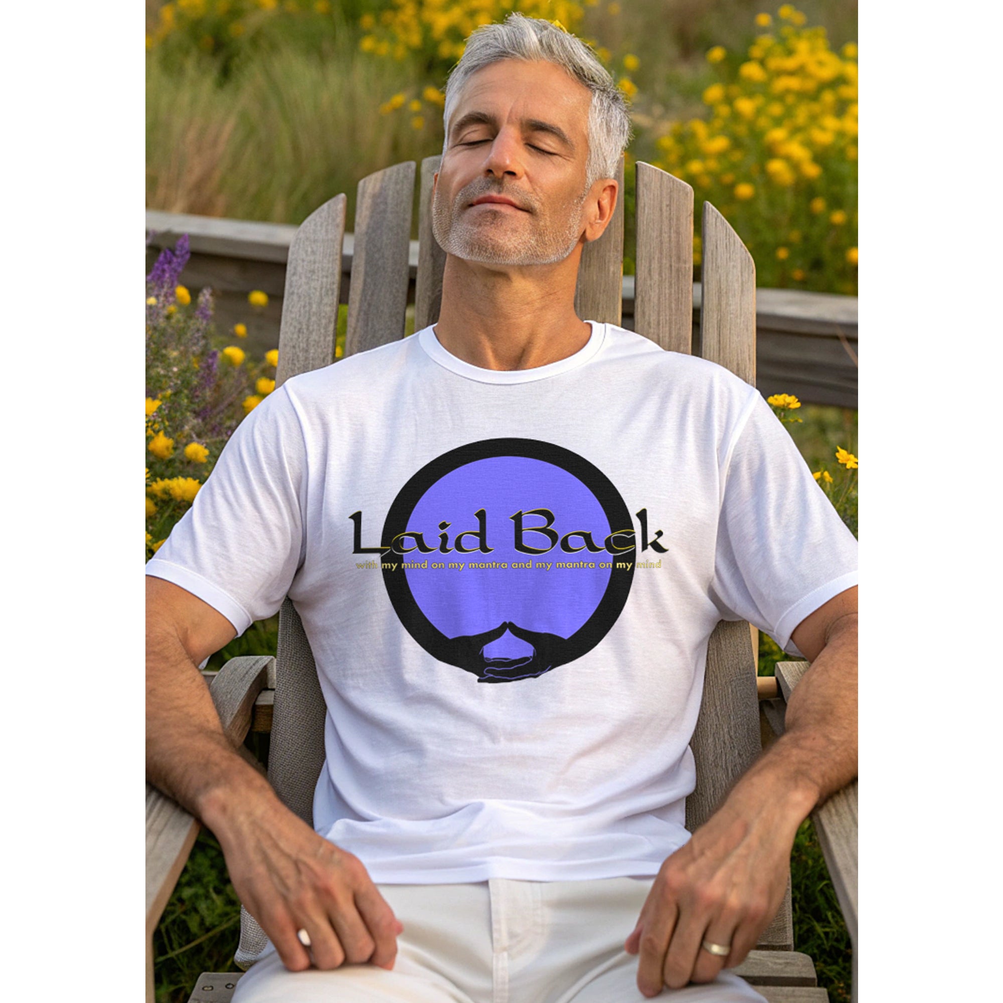Man sitting outdoors in a wooden Adirondack chair wearing a white t-shirt with 'Laid Back' graphic design