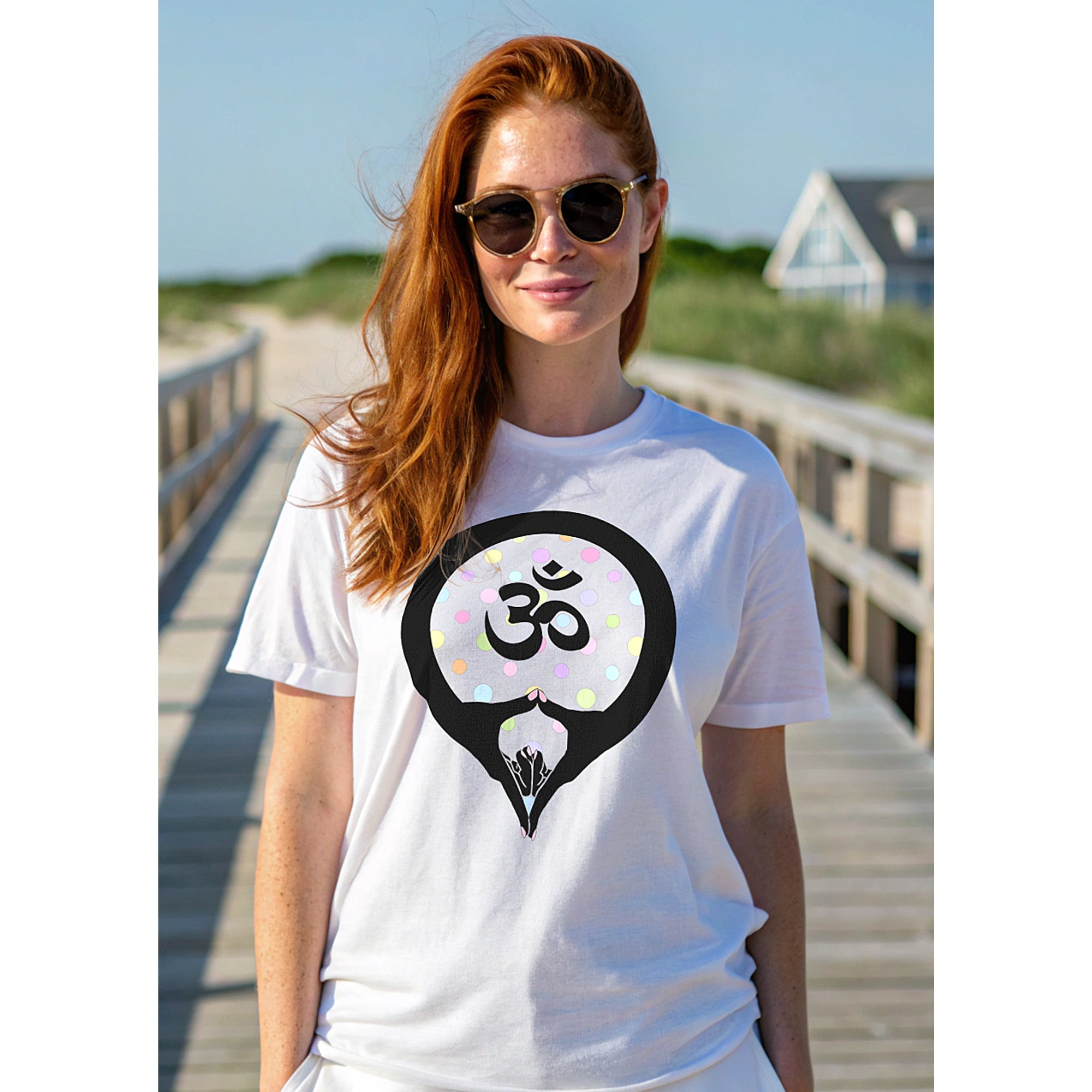 Woman standing outdoors on a wooden boardwalk wearing a white t-shirt with an Om symbol with yoni mudra graphic design